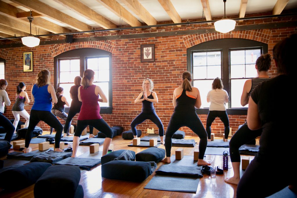 Carol Gray leads a group of pregnant students in a goddess squat pose in a prenatal yoga class at MamaSpace Yoga.