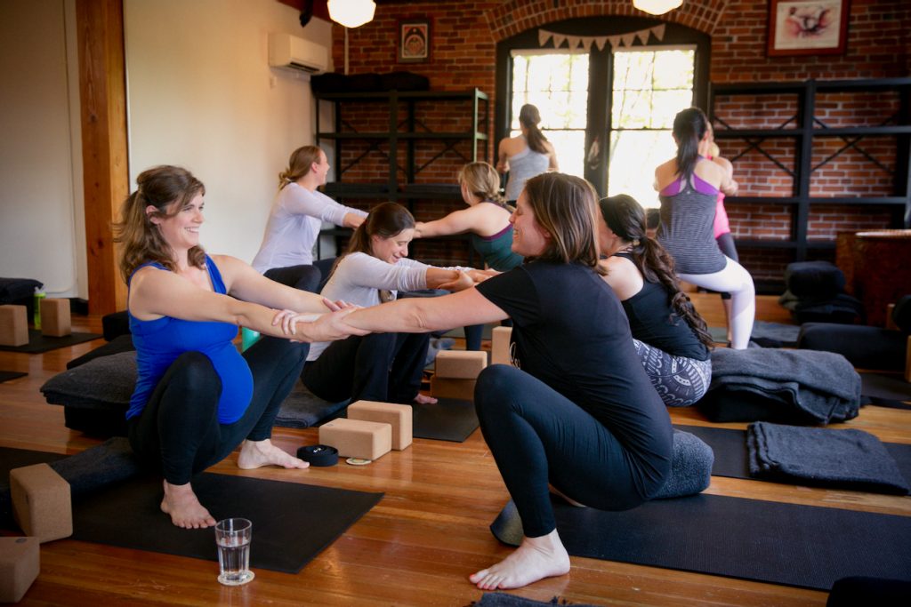 Pregnant students in a prenatal yoga class at MamaSpace Yoga are practiging a pertner squat exercise.