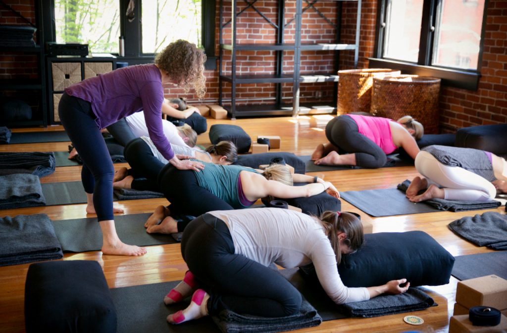 Carol Gray is offering a hands-on adjustnment to a pregnant yoga student in a prenatal yoga class at MamaSpace Yoga. The students are practicing child's pose.