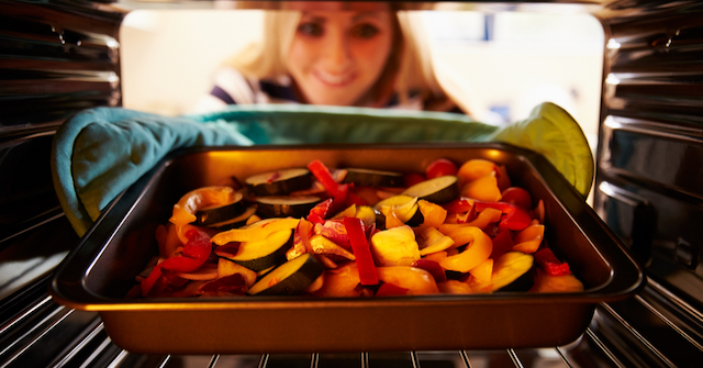 A photo of a women putting a pan of vegetables in the oven for a new family's meal