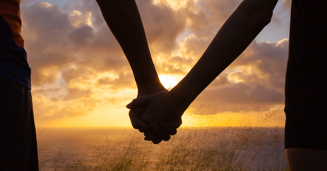 A photo of a couple holding hands silouhetted against a sunset