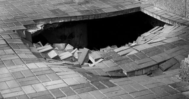 A black and white photo of a hole in a brick sidewalk