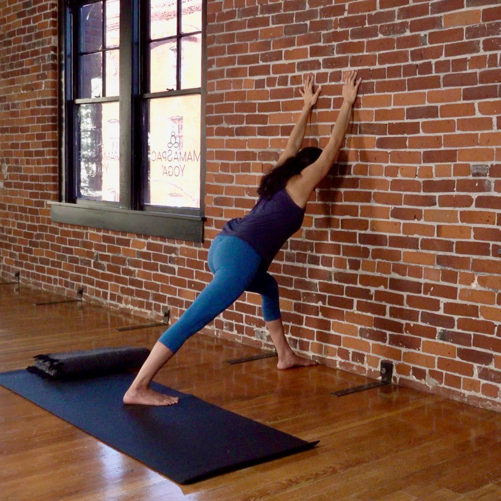 A yoga teacher using the wall as a prop during a prenatal yoga class at MamaSpace Yoga