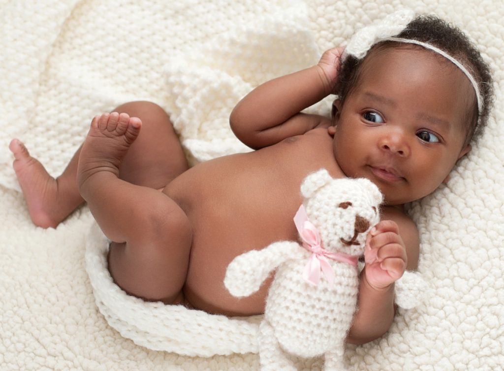 A photo of a baby on a blanket holding a toy