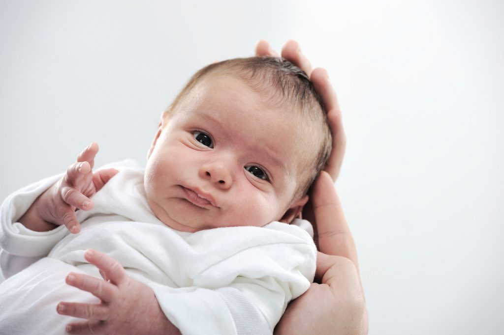 A photo of a small baby held in adult hands