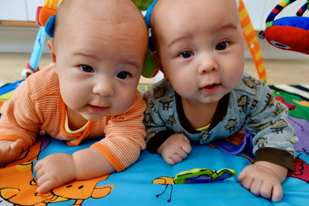 A photo of twin babies in tummy time on a play mat