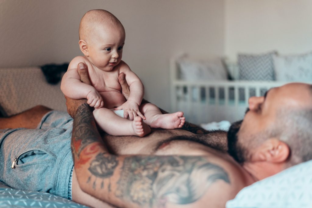 Photo of a man holding a seated baby on his abdomen