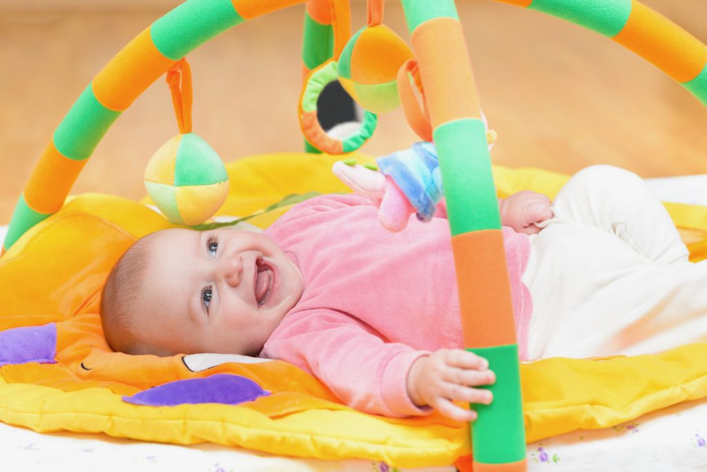 A photo of a baby in supine position playing in a play gym