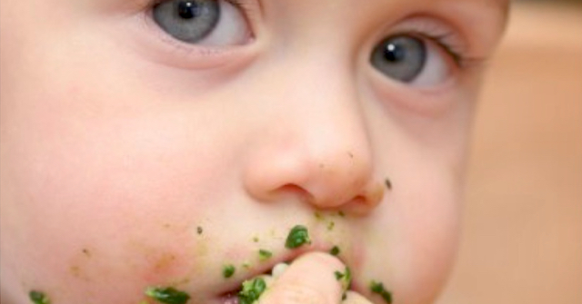 A photo of a baby self-feeding solid food